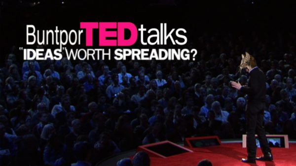 A person with a cat head stands on a red stage facing an audience. Text reads- BuntporTED talks " Ideas worth spreading.