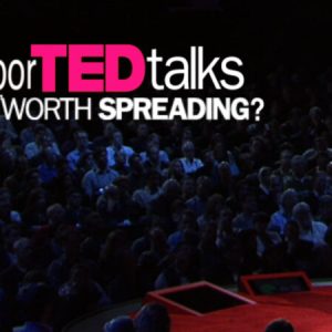 A person with a cat head stands on a red stage facing an audience. Text reads- BuntporTED talks " Ideas worth spreading.