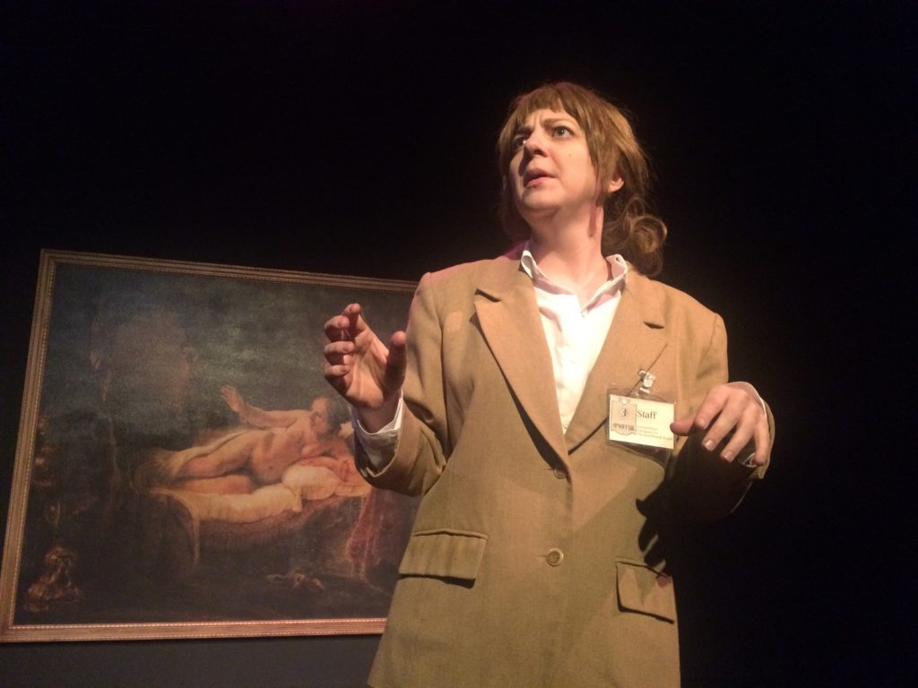 A female art museum security guard stands in front of Rembrandt’s painting of Danae. She’s looking at something in the distance.