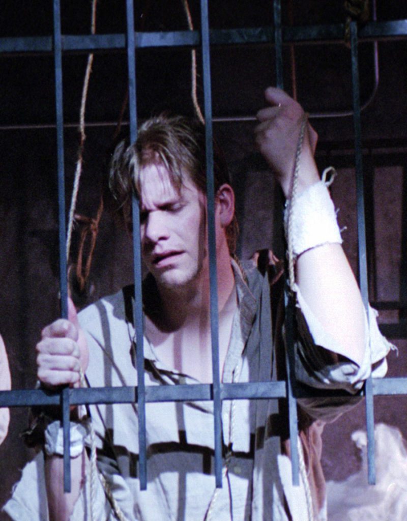 A man behind bars reaches through them dejected.