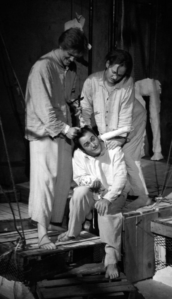 A man and a woman stand above a seated man pushing on his neck with a plaster baton.