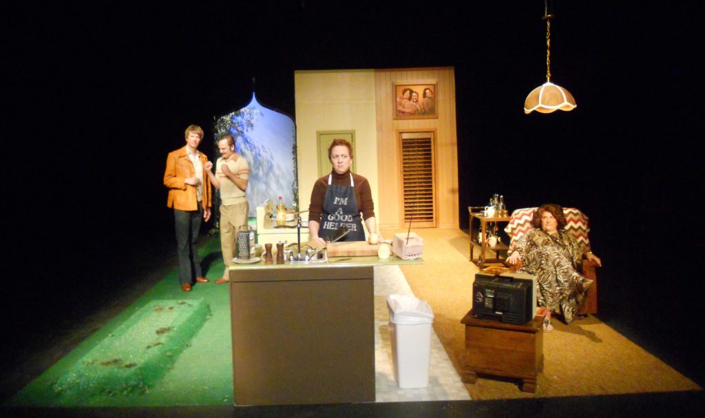 In the center is a miserable-looking woman standing at a sink wearing an “I'm a good helper” apron. To her left, two men stand outside on some astroturf talking. To her right, a woman in a leopard-print caftan sits in a Barca lounger watching TV.