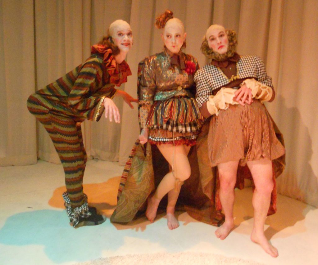 Three clowns stand in the line looking into the camera. The one on the left is turned to the side pushing their obviously enhanced giant butt out. The clown in the middle stands as if they are innocent and the one on the right sticks their belly out and holds it with their hands as if approving and surveying things.