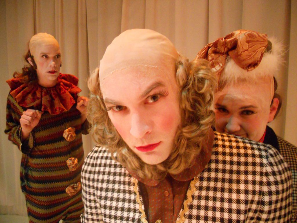 Two clowns in the foreground look as if they have done something bad. The clown behind them looks nervous.