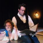 Percy Shelley sits on the edge of a bathtub reading from a book to his wife Mary Shelley who is sitting in the bathtub hanging onto his arm and looking longingly off in the distance.