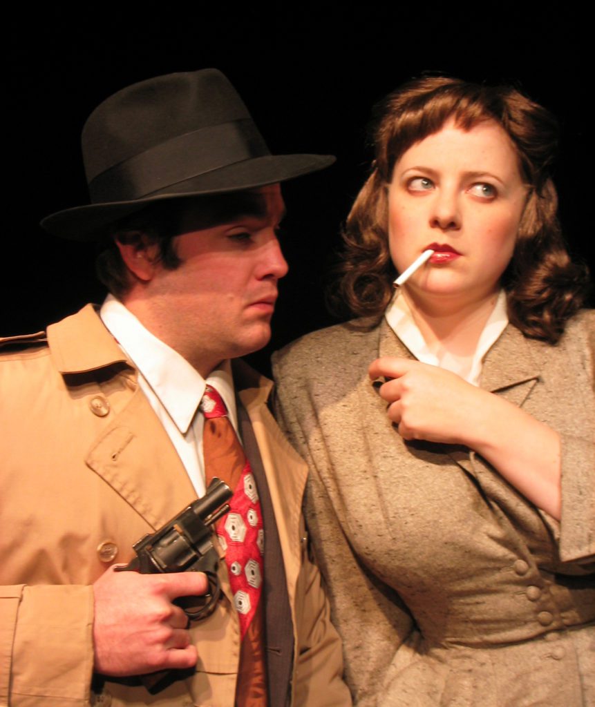 A 1940’s looking detective wearing a fedora hat looks off into the distance dumbfounded with a cigarette hanging out of his mouth while his female partner looks worryingly at him.