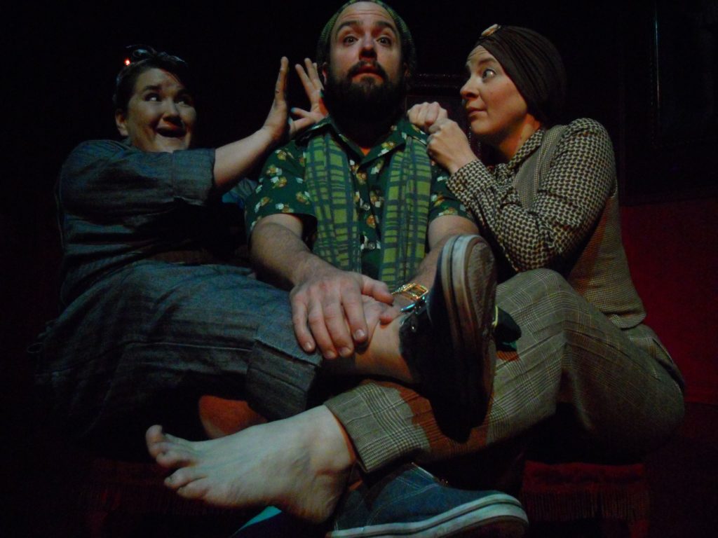 A man sits center wrapped between two women. The women seem to be having fun. The man looks worried.
