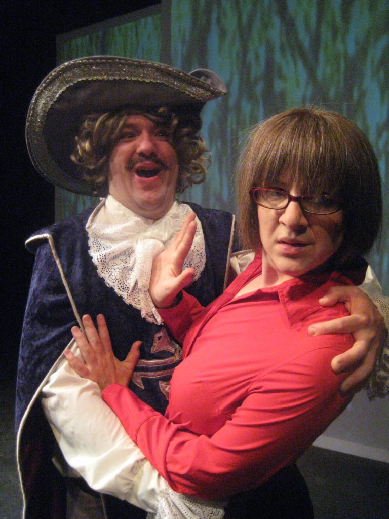 A man dressed as a musketeer happily embraces a woman in a red shirt. She pushes him away.