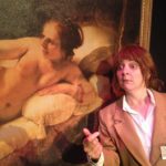 A female art museum security guard stands next to Rembrandt’s painting of Danae. The picture is a close up so we can clearly see both Danae’ face and the museum guards.