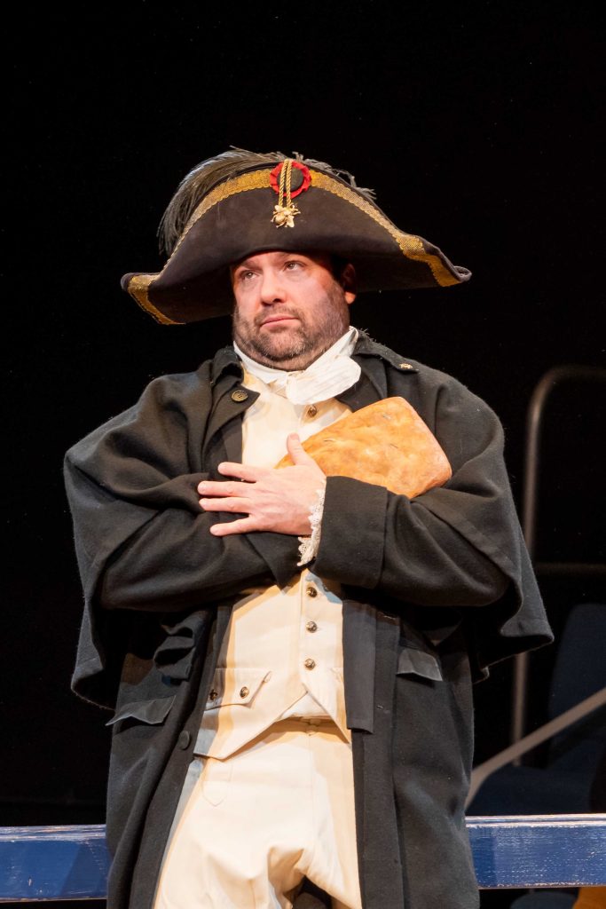 Napoleon stands arms crossed at his chest, showing that one of his hands is focaccia bread