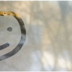 A foggy window with a view of trees and a simple smiley face drawn in the steam.