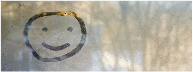 A foggy window with a view of trees and a simple smiley face drawn in the steam.