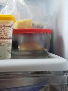 A glass container with a red top that has a white blob inside it, sitting on a refrigerator shelf. 