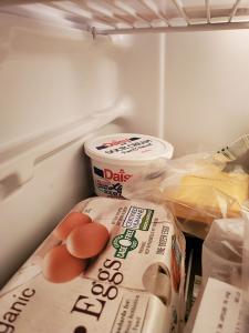 The inside of a fridge. Visible are a container of eggs, a bag with deli cheese and in the back partially buried is a container of sour cream. 