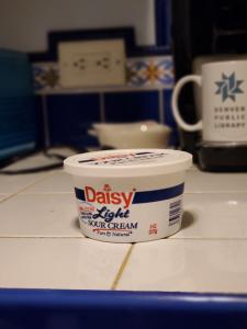 A container of sour cream on the counter. Behind it is a Denver Public Library Mug.