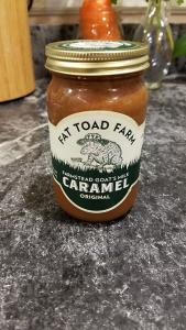 A jar of Caramel Sauce with a white and green lable, on a marble countertop.