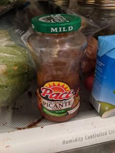 Salsa in a fridge, next to some lettuce and a coconut water. 
