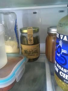 Inside a fridge, behind some tupperware and jars, sits a jar of pickles. 
