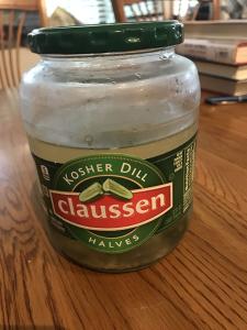 A jar of pickles on a wooden table with book in the background.