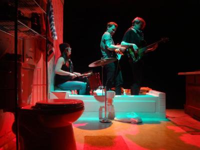 A band plays in a bathtub. The lighting is shadowy and colorful.