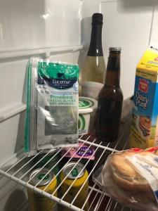 Leaning against the inside of a fridge is a plastic package of very moldy and green provolone cheese. Next to it is a bottle of beer.