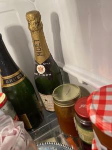 The back corner of a fridge with 2 bottles of champagne and and some jars of condiments.
