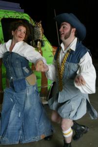 Two people wearing clothes that look Shakespearean, but are made from jeans, are holding hands and skipping in front of a van painted like a forest. There is a plastic owl on the van's side mirror.