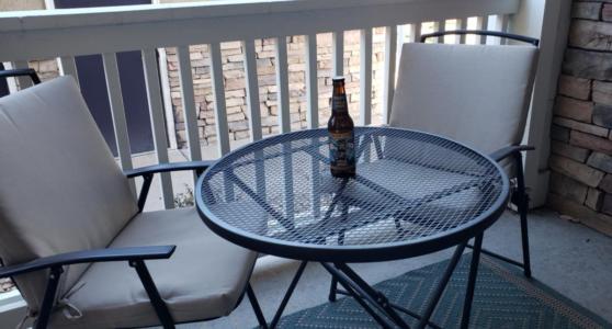 A bottle sits on a metal patio table with two chairs. In the back is a white balcony railing.Is hard cider good forever? 