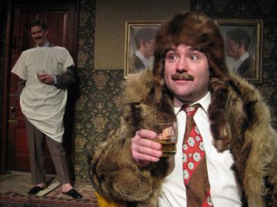 In the foreground a man dressed entirely in furs and wearing a tie holds a glass of whiskey. Behind him, a man dressed in a suit covered by a hospital gown smiles. The two men have the same mustache.