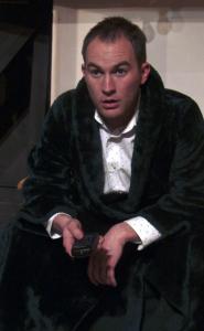 A man wearing a fuzzy green robe stares blankly ahead with a remote control in his hand.