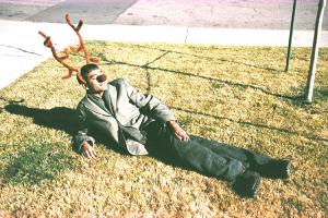 A man, with antlers and deer nose, relaxes in the sun.