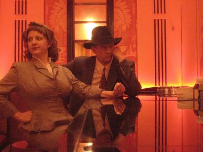 1940’s detectives sit at a bar in an art deco hotel.
