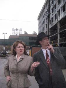 Two 1940’s detectives stand in the middle of a construction site in a dirty town looking confused.