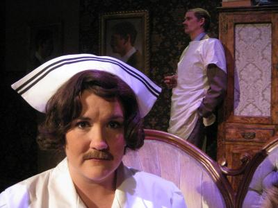 In the foreground a female nurse stares out at the camera. Behind her a man wearing a suit and hospital gown holds a glass of whiskey and ponders his fate. The man and the nurse have the same mustache.