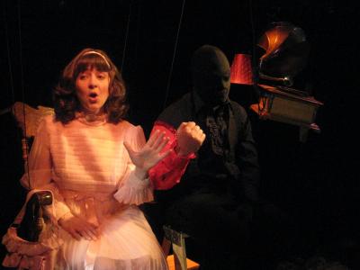 A woman in a pink dress sings a song with a magician’s disembodied arm. Floating in the air next to them is an old fashioned gramophone.