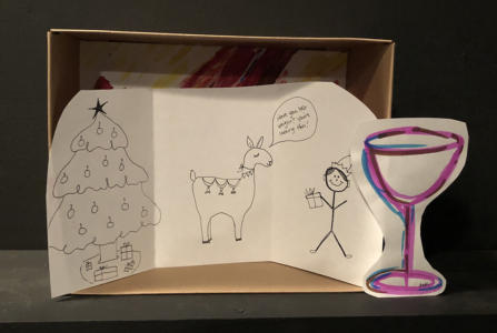 A diorama in a small cardboard box. There is a black-and-white drawing of a fancy llama saying “Have you lost weight? You're looking thin.” to a smiling stick figure. The stick figure has a hat and is holding a present. To the left is a Christmas tree. Leaning on the side of the box, next to the stick figure, is a giant colorful wine glass.