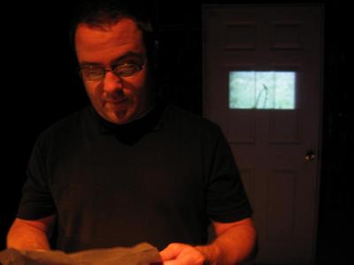 A man with glasses examines a letter. Behind him an image is projected on a white door.