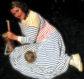 A smiling woman in a striped outfit sits on the floor surrounding by various small instruments. The overall effect is of a silly, cheesy glamour shot.