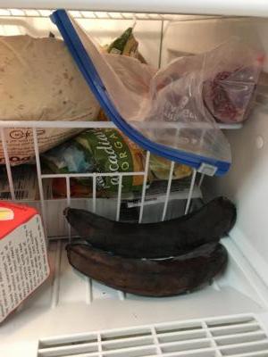 Close-up of the contents of a freezer. Various items are in a white wire basket. In front are two dark bananas.
