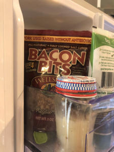 Picture of the inside of a refrigerator door. Some jars surround a bag of Bacon Bits.