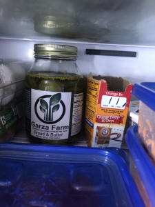 Picture of the inside of a refrigerator. In the foreground are some tupperware containers with blue lids. In the back, a jar of Bread and Butter Pickles and an open box of baking soda.