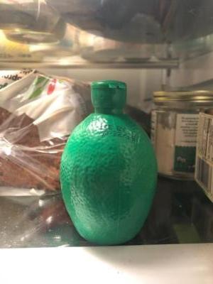 A green, plastic lime sits on a fridge shelf. Behind it are a few jars and a loaf of bread.Forgotten fridge item. Fake lime juice. Still full. 