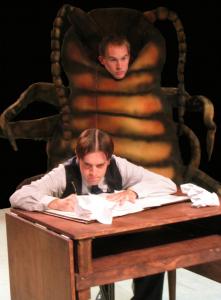 A man writing at a desk concentrates as a large beetle looms behind him. 