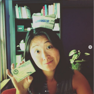 A picture of a society member in their office showing off their BBPSS membership card while wearing a tiny paper hat.