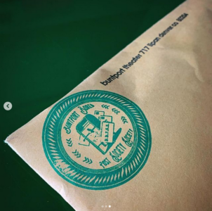 The corner of a white envelope is stamped with the Buntport Bored Post Society Society seal. Next to the seal is the address of the theater.