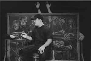 A student sits in front of a large chalkboard. The class seated behind him is drawn in chalk. The chalk students have real arms that poke out from behind the chalkboard.