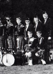 A band dressed in Scottish attire poses for a picture. One of its members looks proud with his antlers and a deer nose.