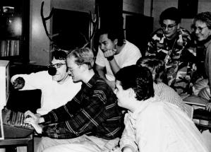 A group of high school students are gathered around a computer. One of the students, with antlers and a  deer nose, points at the screen.