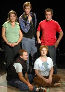 Four people pretending to be serious actors pose for the camera. Three are standing, two are sitting. Most look seriously ahead, but one is gazing at another.