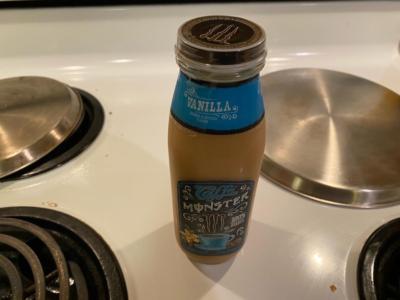 A jar of vanilla flavored coffee drink sits on a white stove. Three of the four burners have metal covers over them.